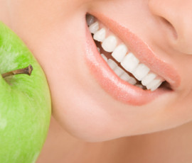 Primer plano de una de una sonrisa saludable de una chica guapa con una dentadura perfecta y una manzana verde a su lado